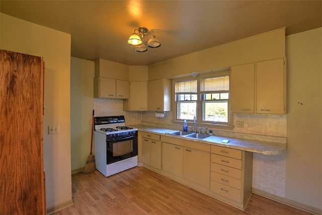 kitchen with an inviting chandelier, sink, white gas range, tasteful backsplash, and light hardwood / wood-style floors