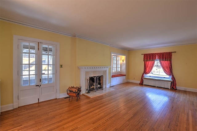 unfurnished living room with hardwood / wood-style floors, french doors, crown molding, a fireplace, and radiator heating unit