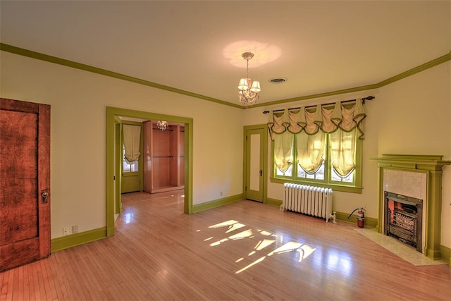 unfurnished living room with radiator, crown molding, a tile fireplace, light hardwood / wood-style flooring, and a notable chandelier