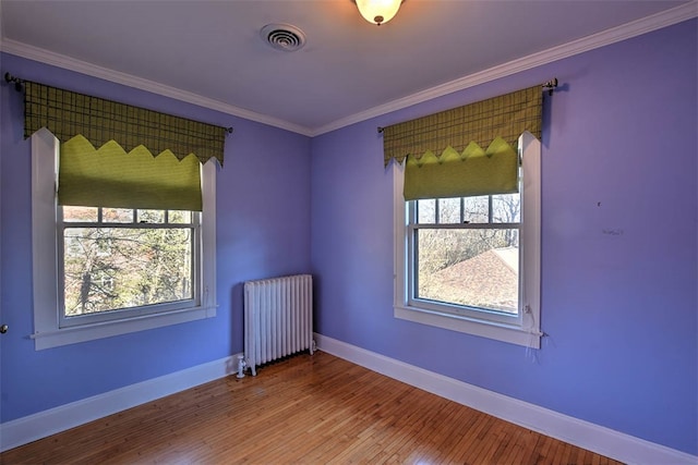 empty room featuring a healthy amount of sunlight, radiator heating unit, and hardwood / wood-style floors