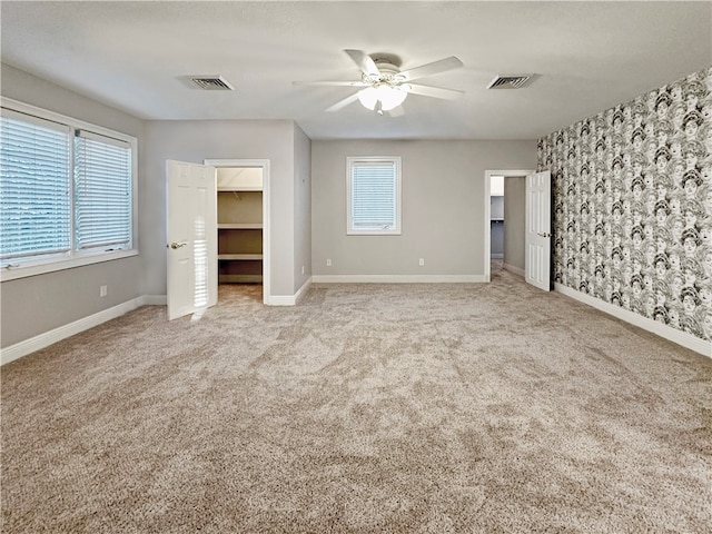 unfurnished bedroom with a walk in closet, ceiling fan, a closet, and light colored carpet