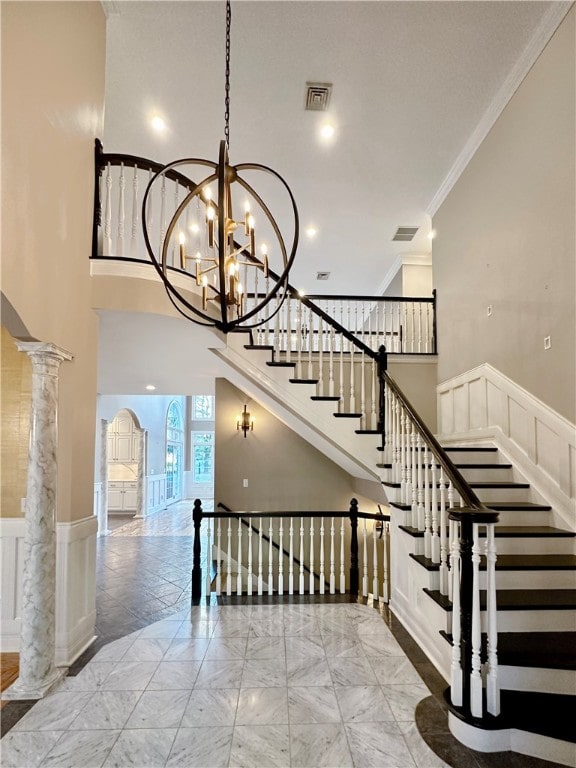 staircase with ornate columns, crown molding, a towering ceiling, and a notable chandelier