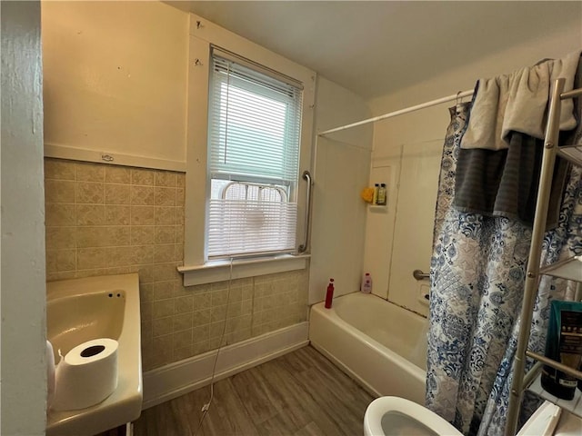 bathroom with toilet, tile walls, shower / bath combination with curtain, and wood finished floors