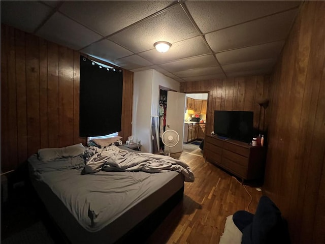 bedroom featuring a paneled ceiling, wood walls, and light wood-style flooring