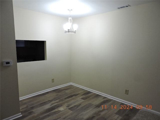 empty room with dark wood-type flooring and a notable chandelier