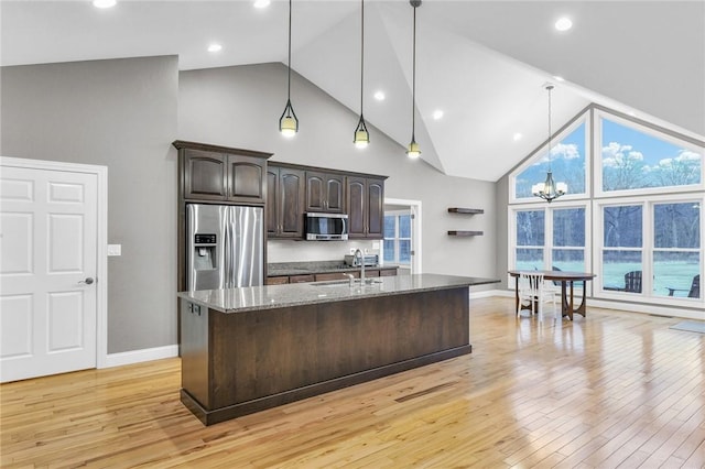 kitchen featuring decorative light fixtures, an island with sink, dark stone counters, dark brown cabinetry, and stainless steel appliances