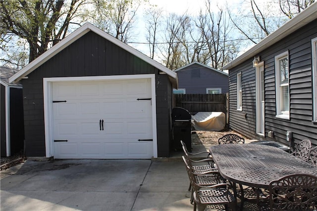 detached garage featuring concrete driveway and fence