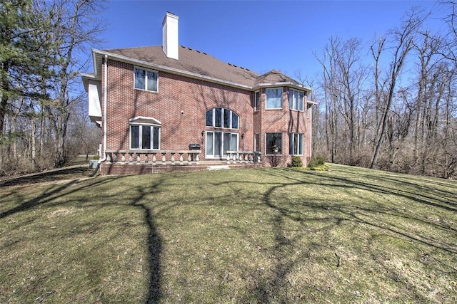 rear view of property featuring brick siding, a lawn, and a chimney