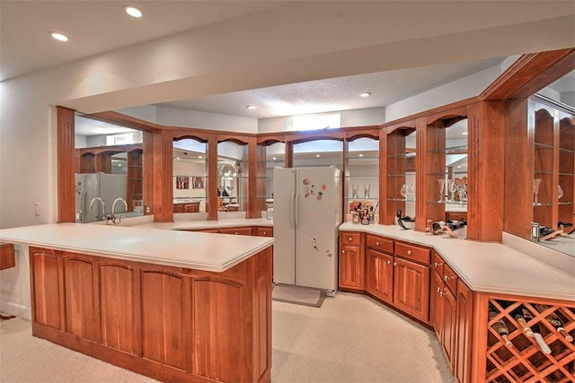 kitchen featuring a peninsula, glass insert cabinets, freestanding refrigerator, and light countertops