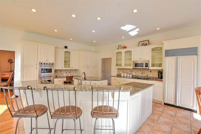 kitchen featuring a breakfast bar area, stone counters, a large island, glass insert cabinets, and appliances with stainless steel finishes