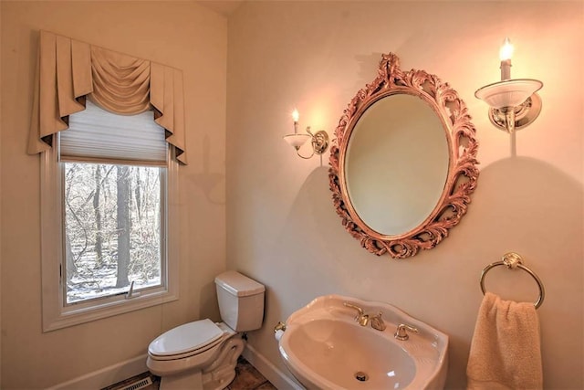 half bathroom featuring plenty of natural light, toilet, baseboards, and a sink