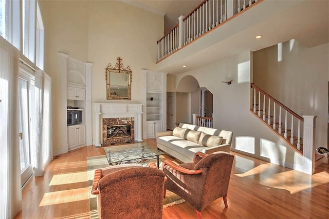 living area with light wood finished floors, a high end fireplace, stairs, a towering ceiling, and arched walkways