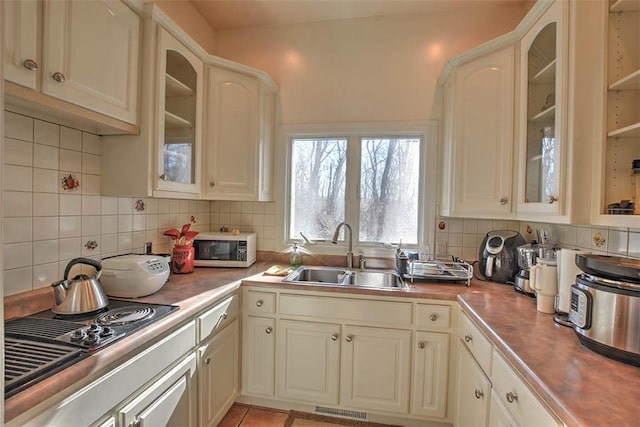 kitchen with white microwave, visible vents, backsplash, black electric cooktop, and a sink