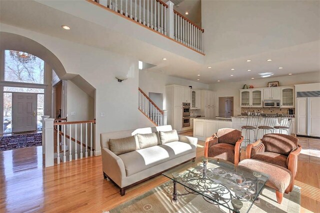 living area featuring light wood-type flooring, a towering ceiling, a fireplace, and french doors