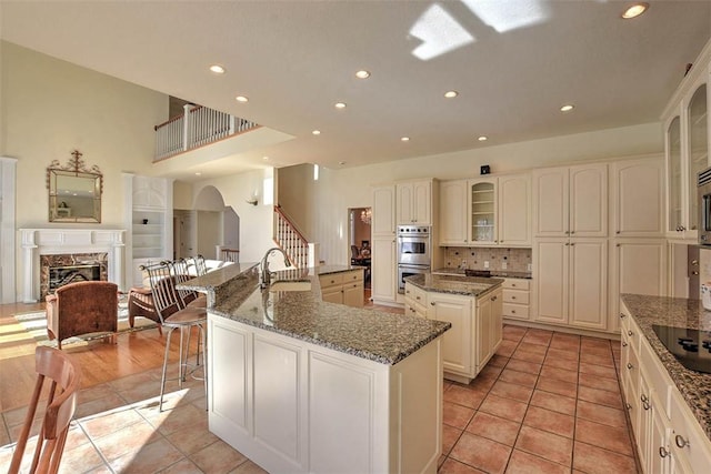 kitchen featuring a sink, a premium fireplace, glass insert cabinets, and a large island with sink