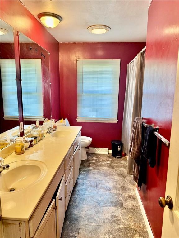 bathroom with a sink, toilet, double vanity, and stone finish flooring