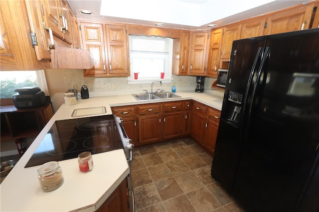 kitchen featuring a raised ceiling, sink, black refrigerator with ice dispenser, and tasteful backsplash