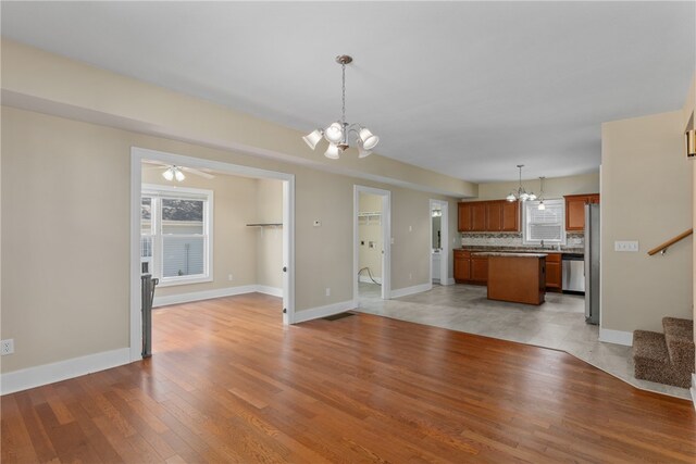 unfurnished living room with ceiling fan with notable chandelier and light wood-type flooring