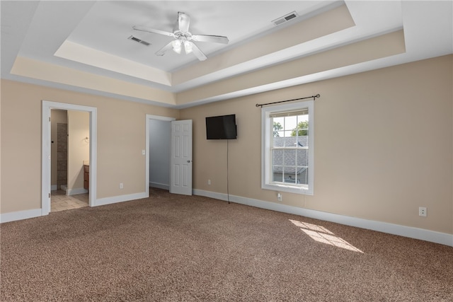 unfurnished bedroom featuring a raised ceiling, ensuite bathroom, and ceiling fan