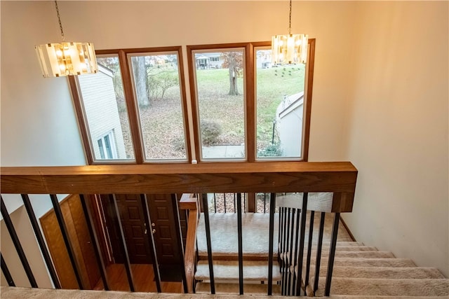 stairs with a wealth of natural light, wood-type flooring, and an inviting chandelier