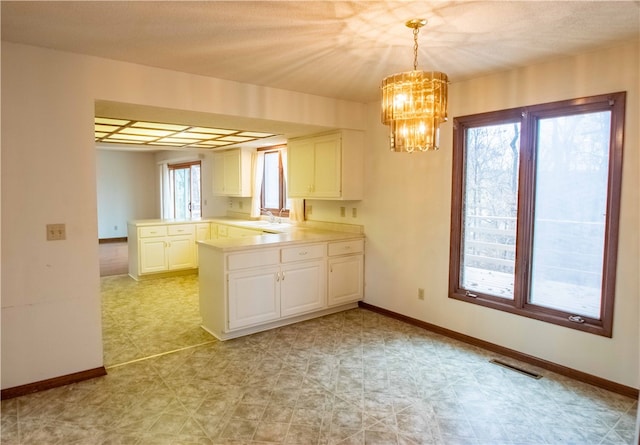 kitchen with kitchen peninsula, a healthy amount of sunlight, sink, white cabinets, and hanging light fixtures