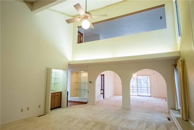 empty room featuring ceiling fan, light colored carpet, a high ceiling, and ornamental molding