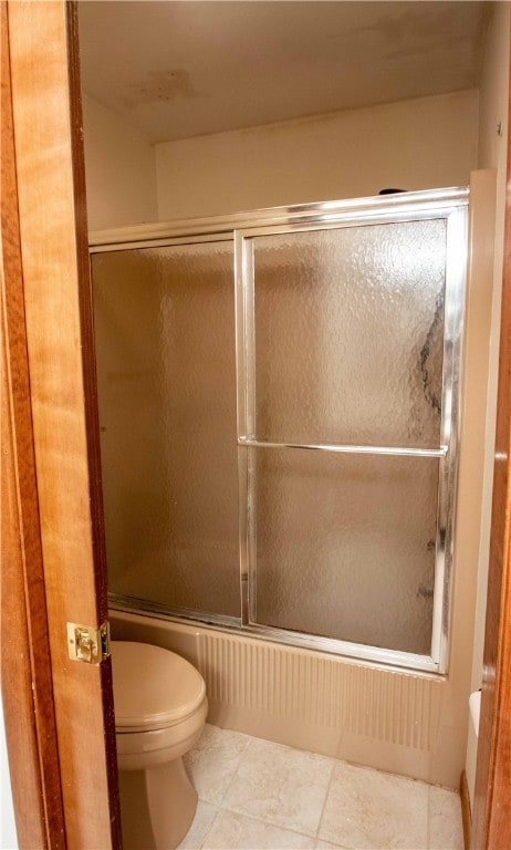 bathroom with tile patterned flooring, toilet, and combined bath / shower with glass door