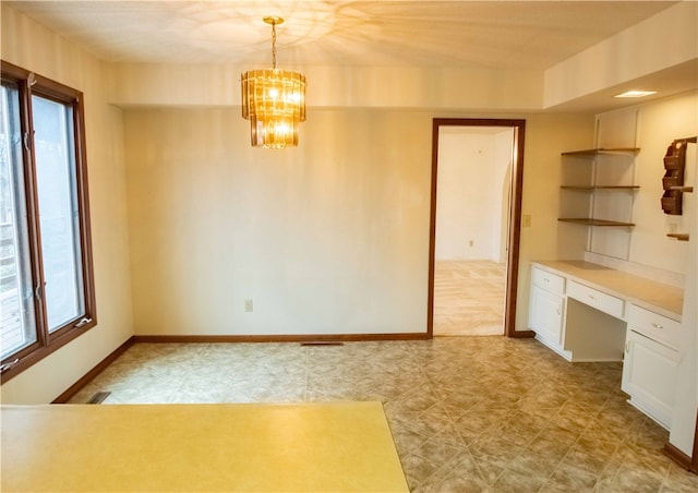 unfurnished dining area with built in desk and an inviting chandelier