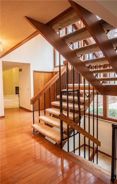 stairway featuring hardwood / wood-style floors, a textured ceiling, and high vaulted ceiling