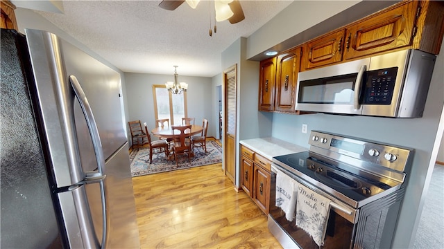 kitchen with light countertops, light wood-style flooring, appliances with stainless steel finishes, brown cabinetry, and a textured ceiling