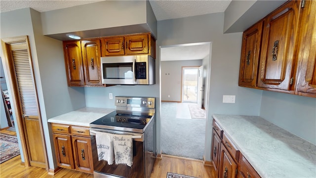 kitchen featuring a textured ceiling, stainless steel appliances, brown cabinetry, and light countertops