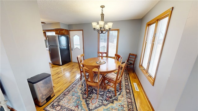 dining space featuring light wood-type flooring, an inviting chandelier, visible vents, and a textured ceiling