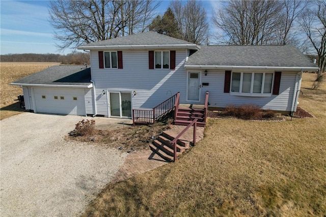 split level home featuring a garage, gravel driveway, a shingled roof, and a front lawn