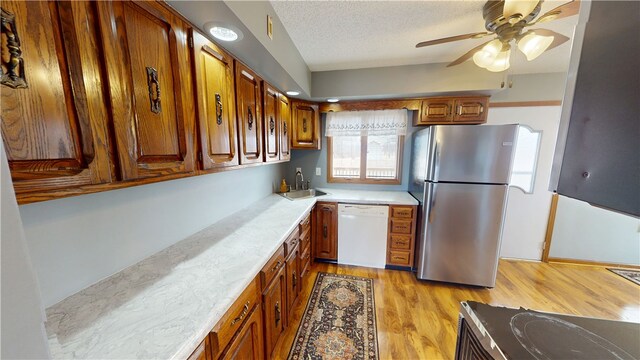 kitchen featuring light wood finished floors, light countertops, freestanding refrigerator, a sink, and dishwasher