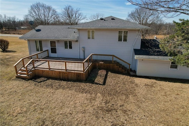 back of house featuring a shingled roof, a deck, and a lawn