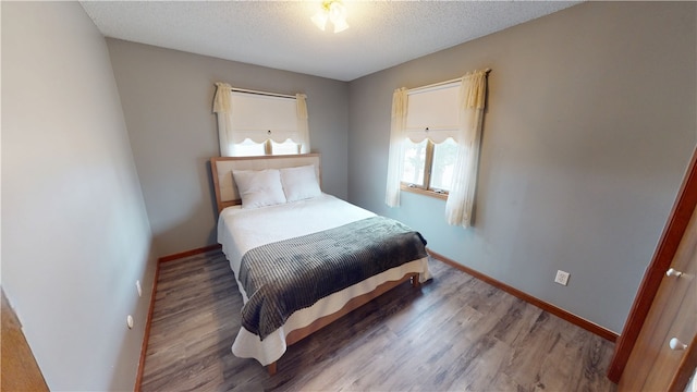 bedroom with a textured ceiling, baseboards, and wood finished floors