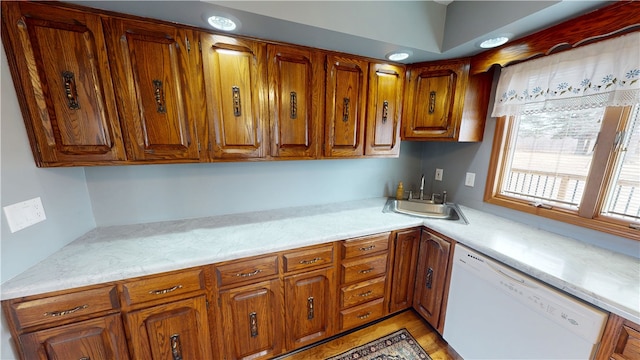 kitchen featuring light countertops, brown cabinetry, white dishwasher, and a sink