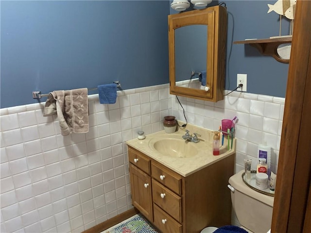 bathroom with toilet, wainscoting, vanity, and tile walls