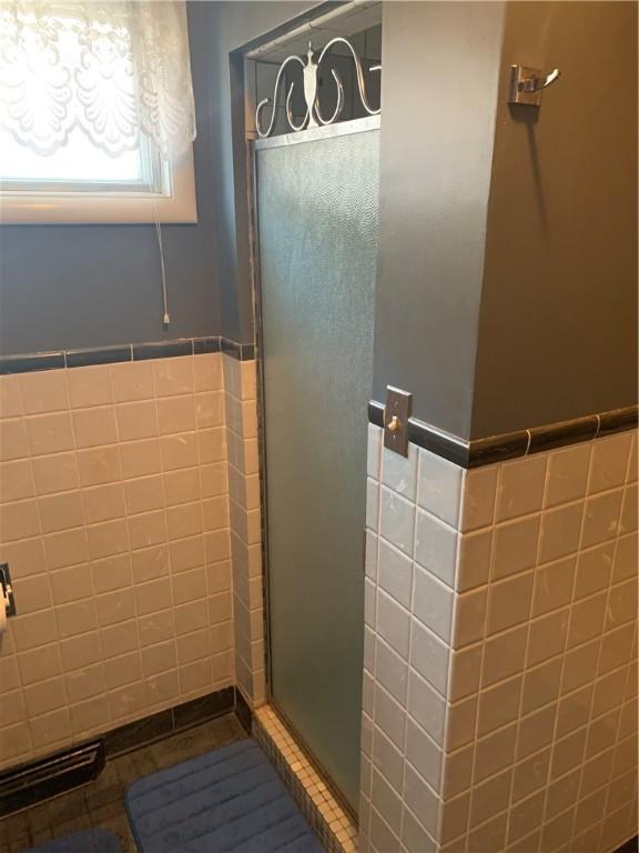 bathroom featuring a stall shower, wainscoting, tile walls, and tile patterned floors