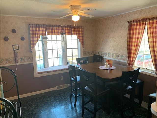 dining space with ceiling fan, visible vents, baseboards, wallpapered walls, and crown molding