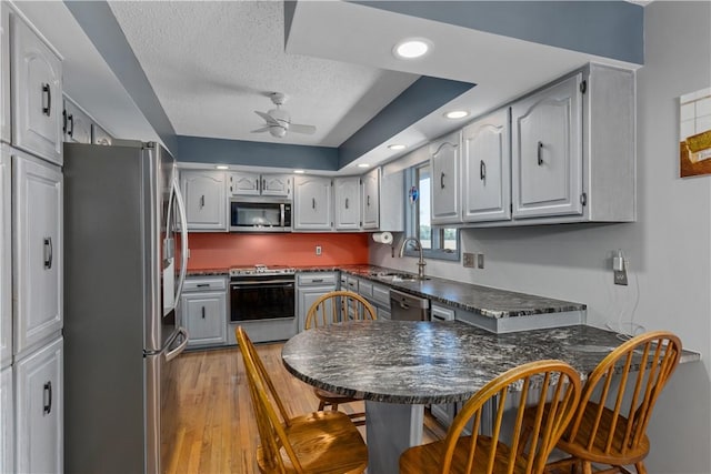 kitchen featuring appliances with stainless steel finishes, a sink, ceiling fan, dark countertops, and a textured ceiling