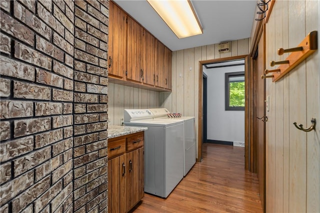 washroom with washing machine and dryer, cabinet space, light wood-style floors, and wood walls