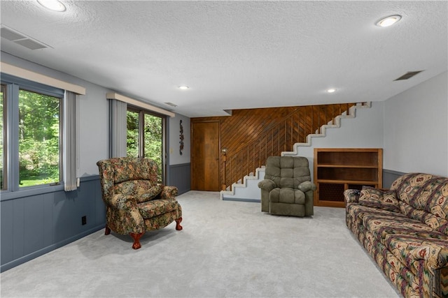 living room featuring stairs, a textured ceiling, carpet flooring, wooden walls, and recessed lighting