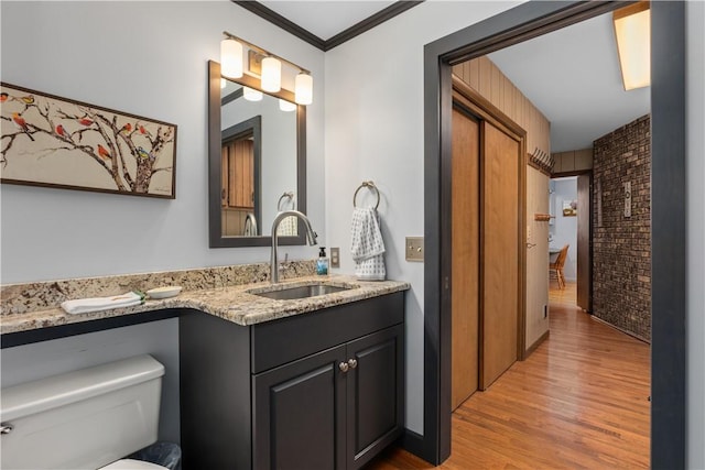 bathroom featuring wood finished floors, double vanity, brick wall, toilet, and crown molding