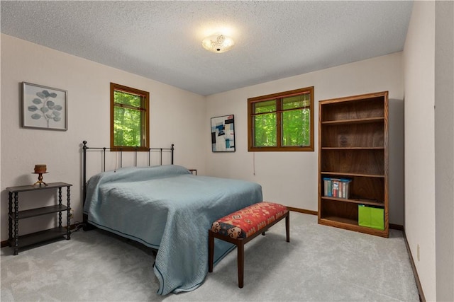 bedroom featuring light colored carpet, a textured ceiling, and baseboards