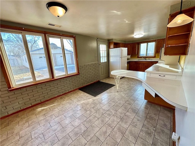 kitchen featuring brick wall, a sink, visible vents, light countertops, and freestanding refrigerator