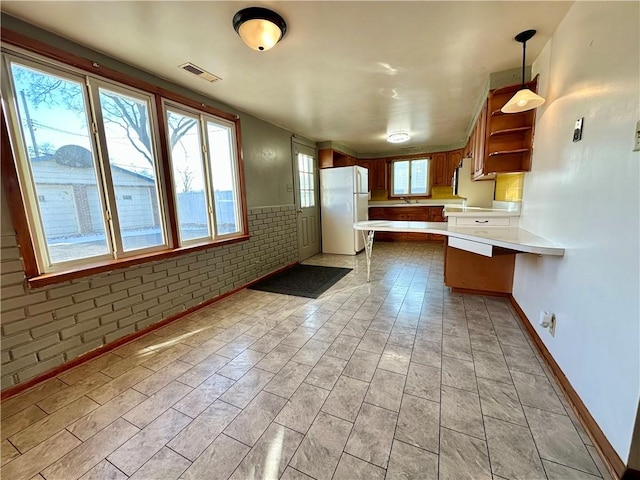 kitchen featuring open shelves, light countertops, visible vents, freestanding refrigerator, and a peninsula