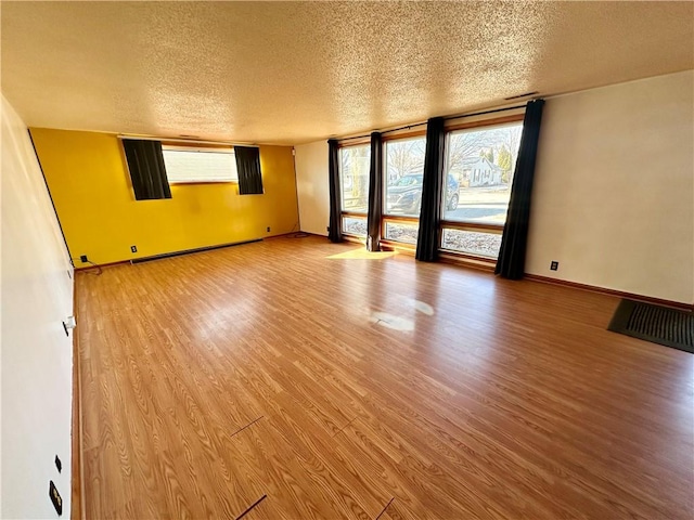 empty room featuring light wood finished floors, baseboards, baseboard heating, and a textured ceiling