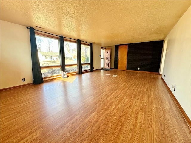 unfurnished living room with visible vents, a textured ceiling, baseboards, and wood finished floors