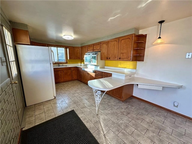 kitchen with oven, a peninsula, light countertops, freestanding refrigerator, and brown cabinetry